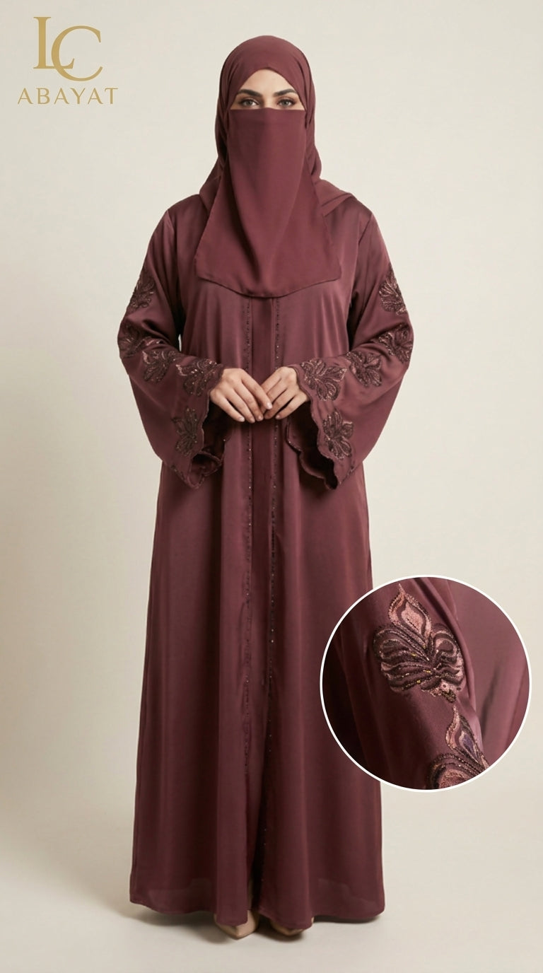 A woman wearing a deep burgundy abaya with matching hijab and lace-embroidered sleeves, shown against a plain beige studio background. A circular inset highlights the embroidered sleeve detail, and the LC Abayat brand logo appears in the top left.