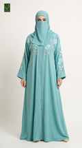 A woman modeling a long, flowing sky blue abaya with floral embroidery on the chest and sleeves, paired with a matching headscarf and face veil, against a plain light background.