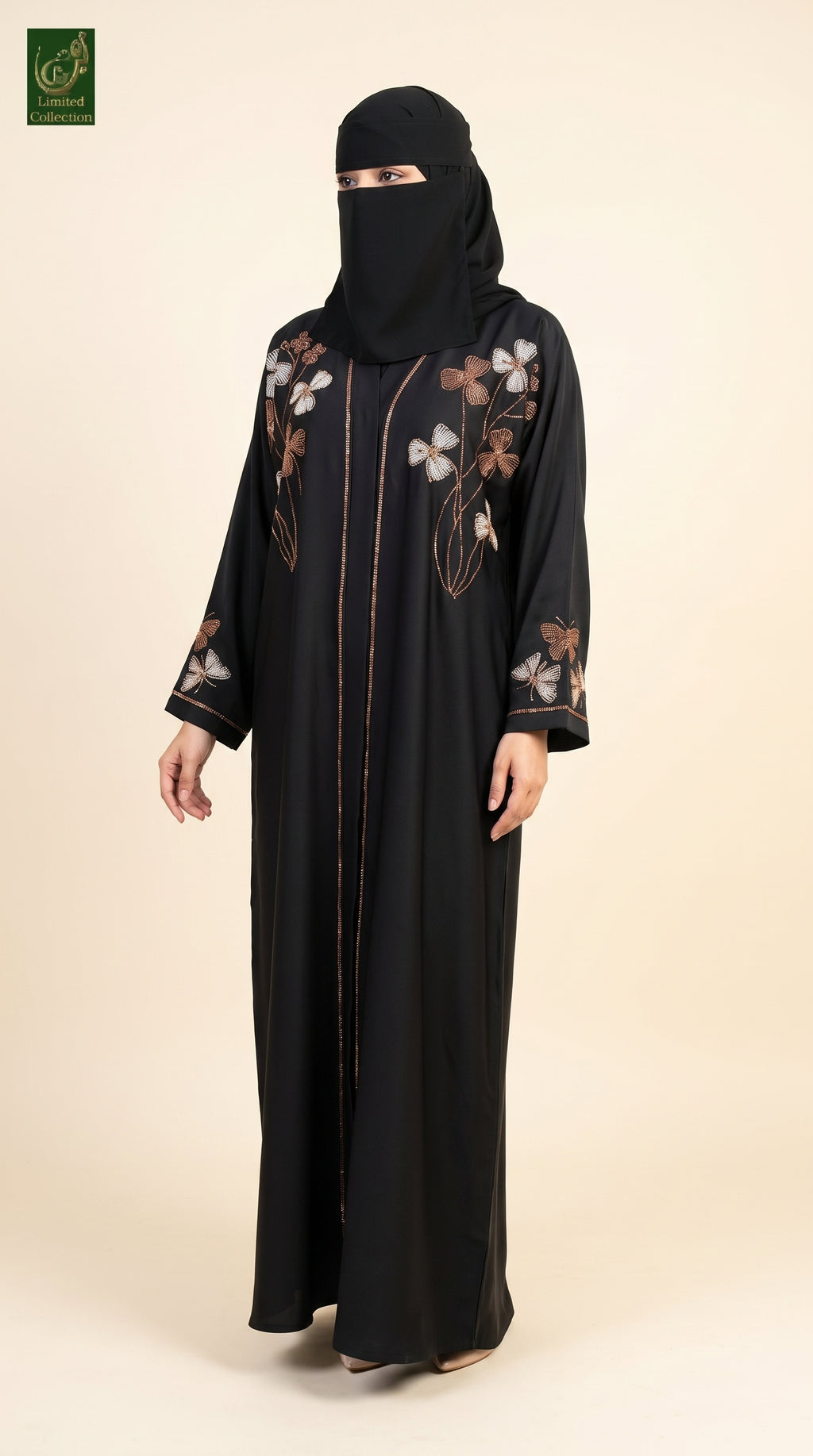 A woman wearing a black abaya with floral embroidery on the chest and sleeves, paired with a matching black niqab, standing against a solid beige background.