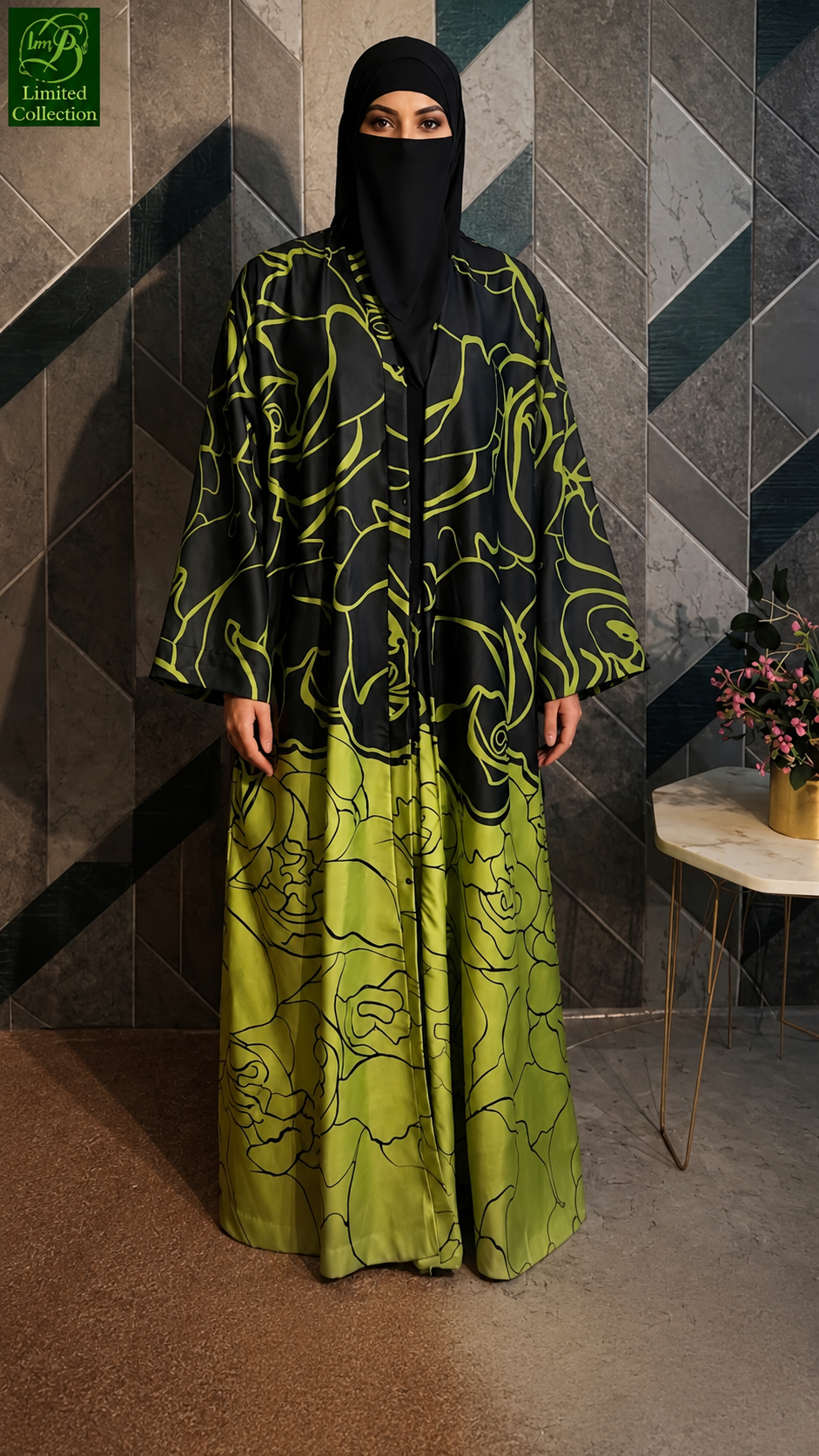 A woman wearing a black and olive green rose line patterned abaya with a matching black hijab stands in front of a geometric tiled wall. The abaya features a black base with a vibrant olive green abstract floral pattern, and a solid olive green lower skirt section.