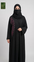 A woman wearing a black abaya with a pink embroidered leaf design on the sleeve, paired with a black hijab, standing against a light gray background. A 'Limfeet Collection' logo is visible in the top left corner.