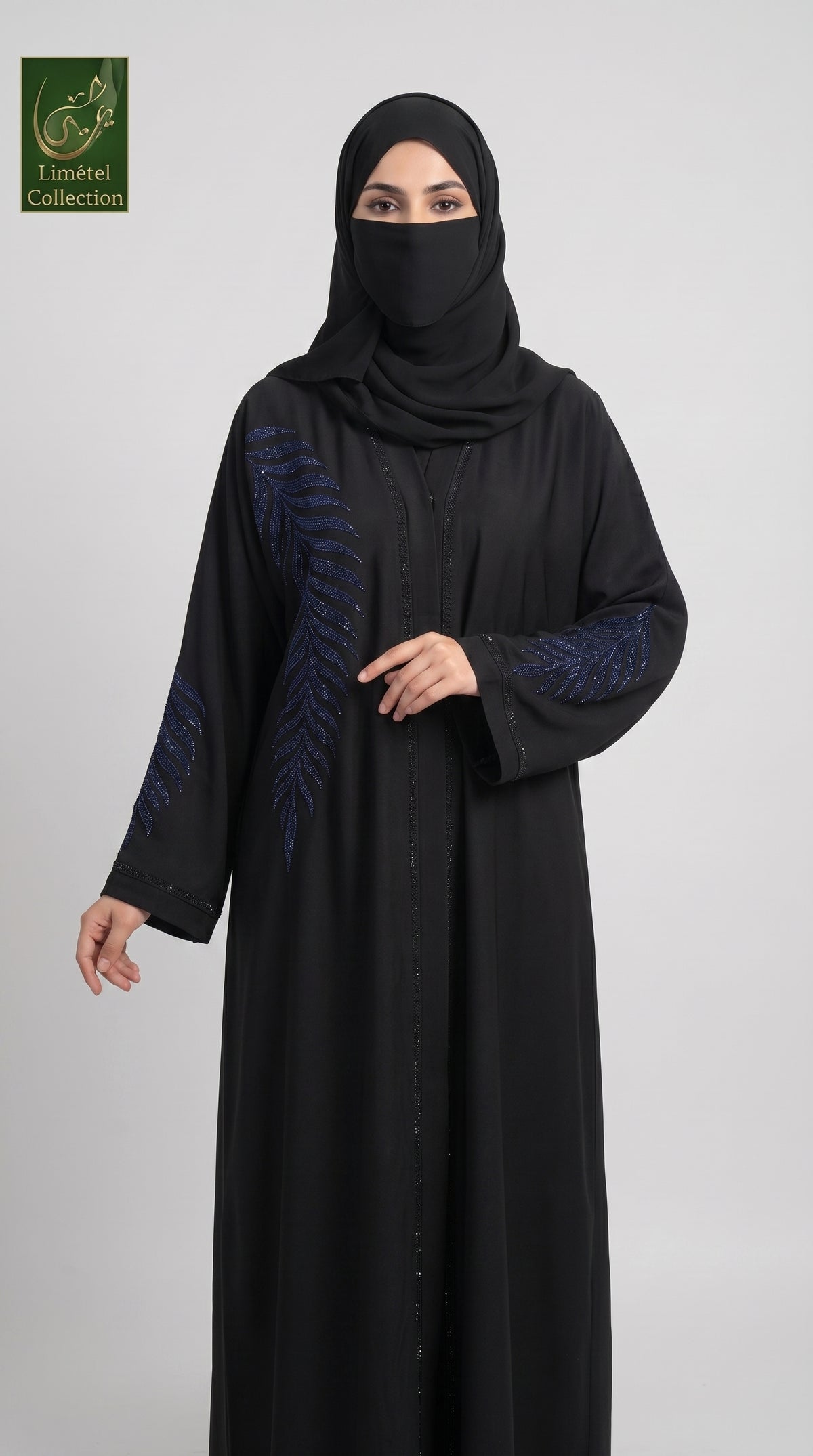 A woman wearing a black abaya with dark blue embroidered leaf patterns on the sleeves, paired with a matching black hijab, shown against a light gray studio background. The 'Limfeet Collection' logo is visible in the top-left corner.
