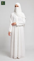 A woman wearing a long white abaya dress with a matching white hijab and face veil, standing against a light gray studio background. The logo for 'Al-Arayat' is visible in the top left corner.