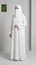 A woman wearing a white abaya and matching hijab stands in a studio setting with a light gray background. A green 'Limited Collection' logo is visible in the top-left corner.