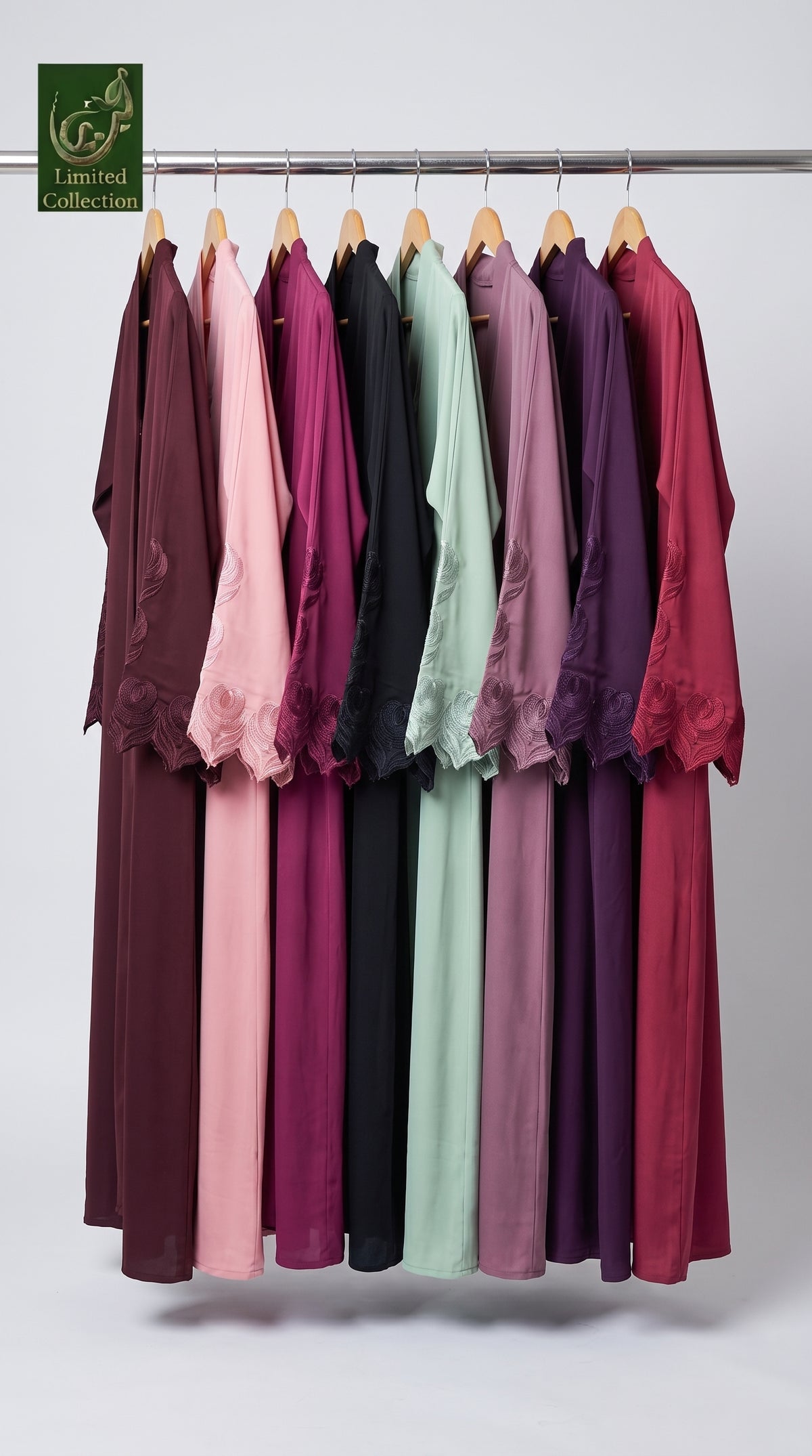 A set of long flared, front-open, colorful stonework abayas hanging on a metal rack against a light gray studio background. The collection features multiple solid colors including deep burgundy, dusty pink, black, sage green, lavender, and plum.