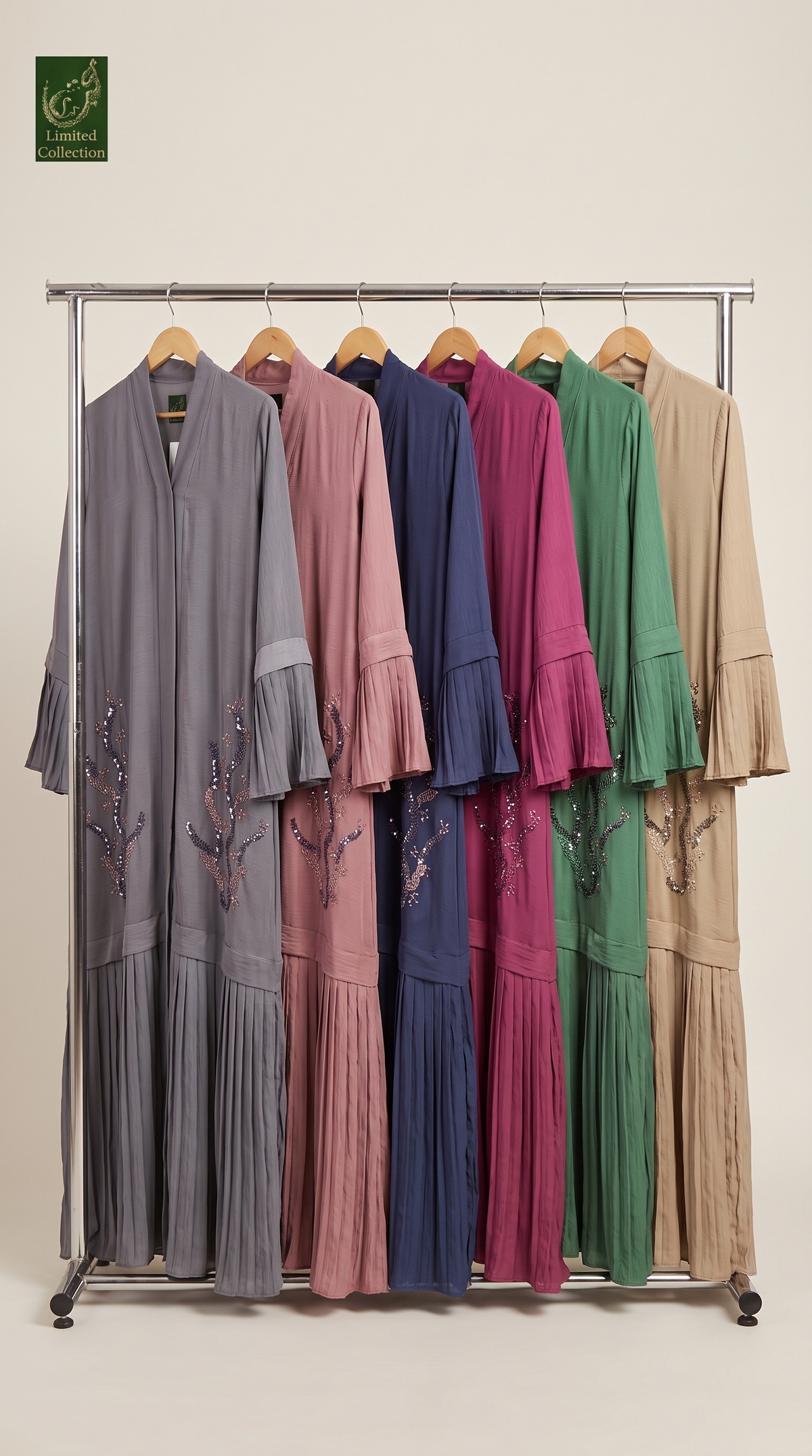 A metal clothing rack displaying six long modest abayas in different colors: gray, dusty pink, navy blue, magenta, emerald green, and beige. Each dress features a draped front, layered ruffle sleeves, and embroidered floral details near the lower front.