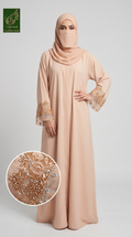 A woman modeling a peach-beige abaya with matching hijab and a face veil, featuring ornate gold and silver beadwork on the sleeves. A circular inset highlights the detailed embroidery.
