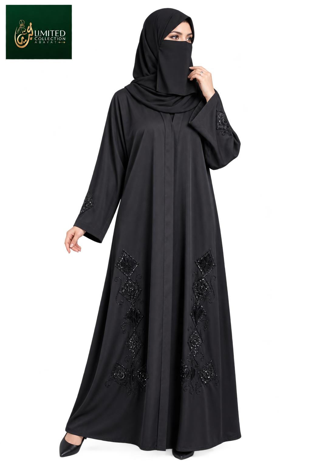 A woman modeling a black full-length abaya with matching hijab and black shoes against a plain white background. The abaya features decorative black embroidered patterns near the lower hem and sleeve cuffs.