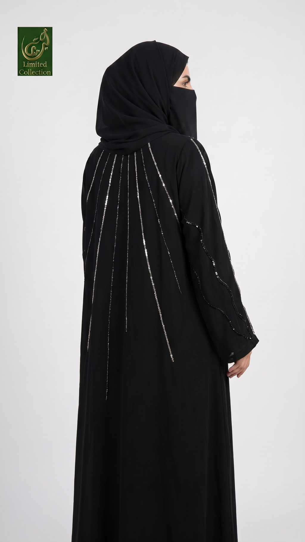 A woman wearing a black abaya and matching hijab, shown from the back against a light gray studio background. The abaya features vertical silver beaded fringe details running from the shoulders down the back and along one sleeve.