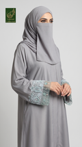 A woman wearing a light gray modest cutdana abaya with a matching hijab and a face veil, featuring light blue embroidered lace cuffs, posed against a neutral gray background. A 'Limited Collection' logo is visible in the top-left corner.