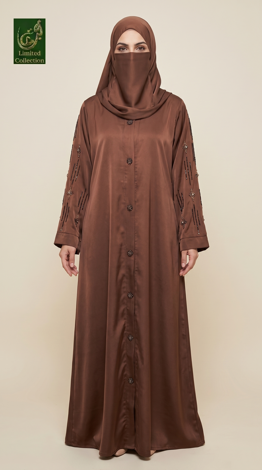A woman wearing a long brown abaya with matching hijab, standing against a plain beige studio background. The abaya has a satin-like sheen, a button front, and decorative embroidered details on the sleeves.