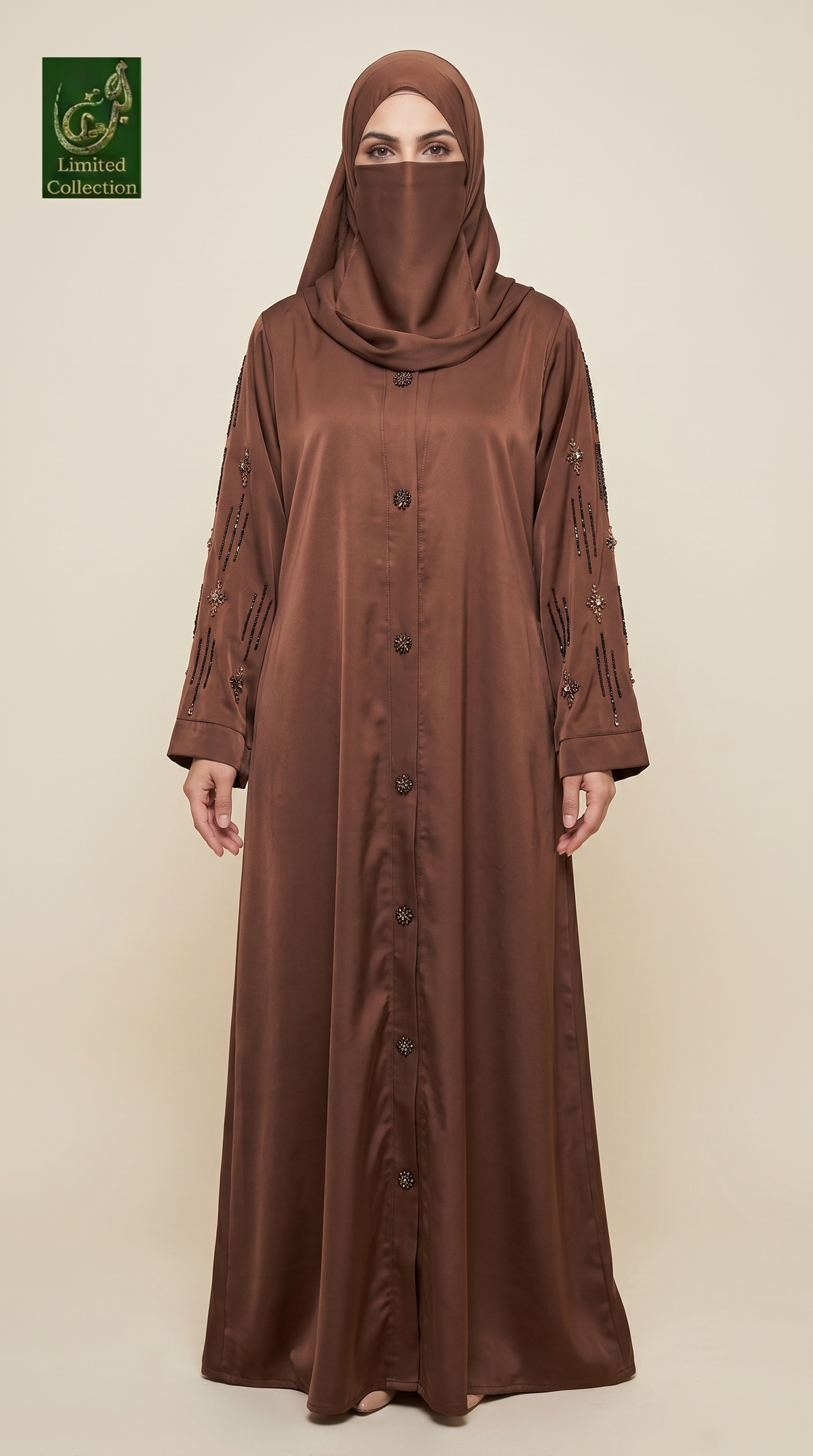 A woman wearing a long brown abaya with matching hijab, standing against a plain beige studio background. The abaya has a satin-like sheen, a button front, and decorative embroidered details on the sleeves.