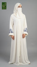A woman wearing a long white abaya with blue leaf embroidery on the cuffs and a matching white hijab, standing against a solid gray studio background. A green 'Limited Collection' logo is visible in the top-left corner.