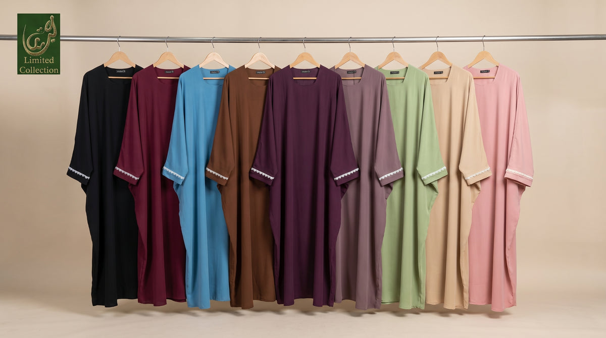 A row of loose, long-sleeve tunic-style front open butterfly abaya with lace cuffs on wooden hangers against a plain beige studio background. The garments come in multiple solid colors including black, burgundy, light blue, brown, plum, mauve, sage green, beige, and light pink.