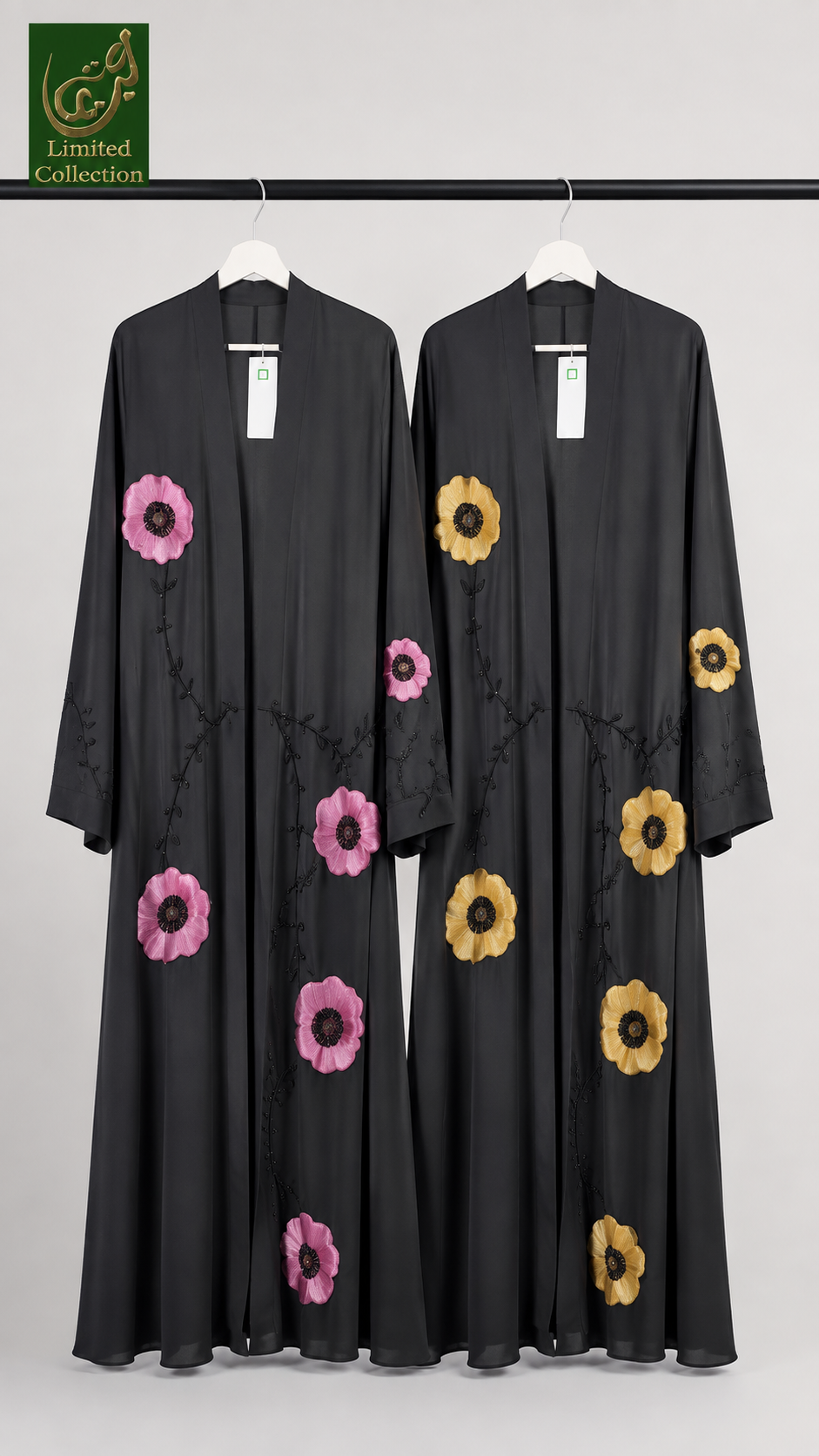 Two long black abayas hanging on a black clothing rack against a light gray background. The abaya on the left features pink flowers with dark centers, and the abaya on the right features yellow flowers with dark centers.