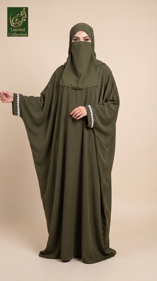A woman wearing a flowing olive green abaya with a matching hijab and a small silver mirror embellishment on the sleeve, standing against a solid beige background. A logo for 'Limited Collection' is visible in the top-left corner.