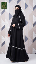 A woman wearing a black full-length abaya with white lacing details and a matching black hijab, standing against a geometric patterned wall. A logo for 'Limited Collection' is visible in the top-left corner.
