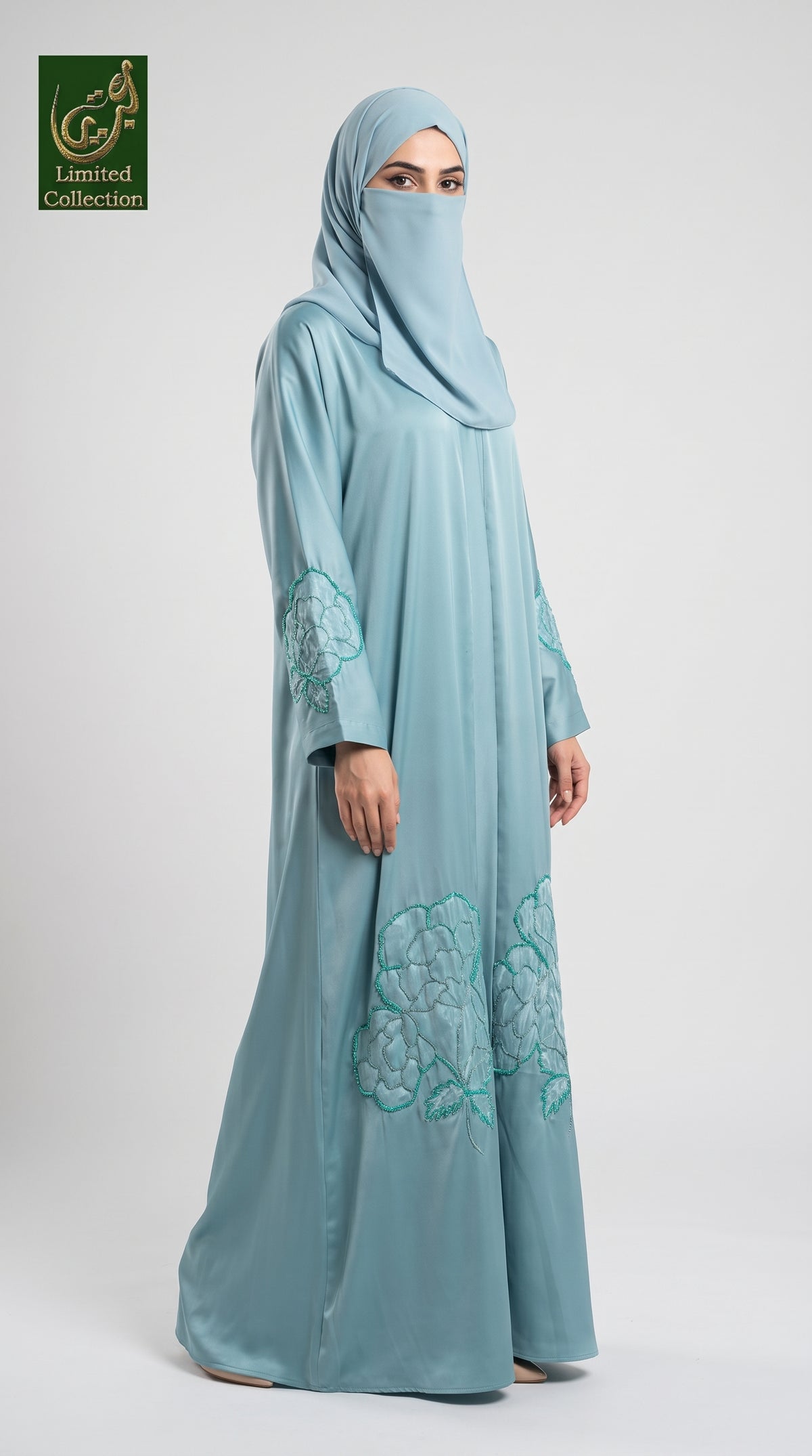 A woman modeling a light blue modest abaya with cutdana handwork consisting of a long abaya with teal floral embroidery and a matching hijab, shown against a plain light gray studio background. A 'Lamored Collection' logo is visible in the top-left corner.