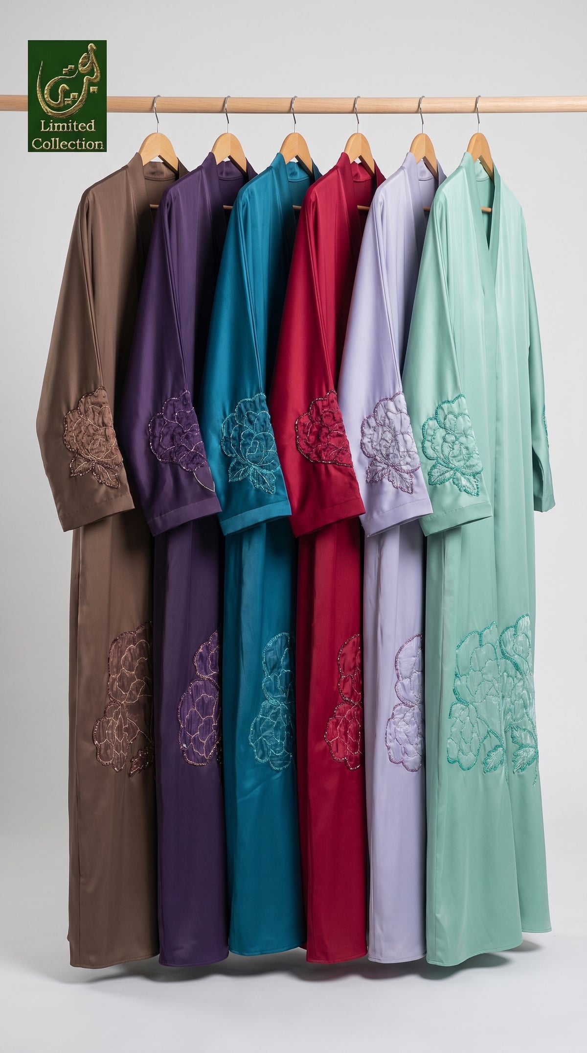 Six long-sleeve traditional abayas in brown, purple, teal, red, lavender, and mint green hang on a wooden rack against a light gray background. Each robe features embroidered floral patterns on the lower body and cuffs.