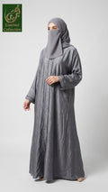 A woman wearing a long, flowing gray abaya with a matching gray hijab, standing against a light gray studio background. A green 'Limited Collection' logo is visible in the top-left corner.